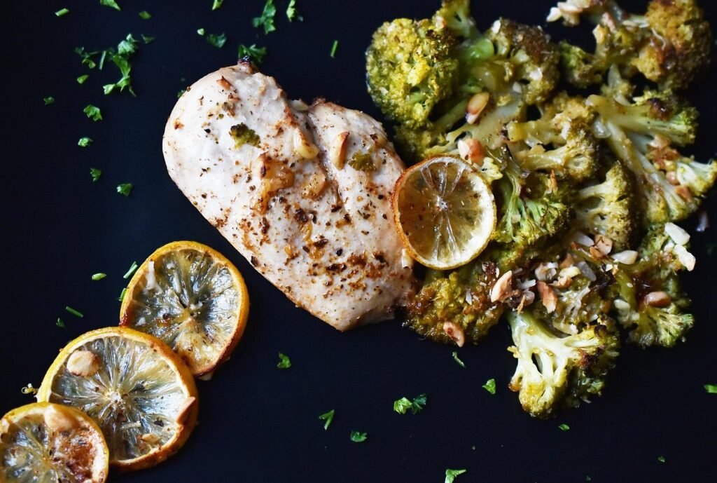 Baked chicken breast with lemon slices and roasted broccoli on a dark surface