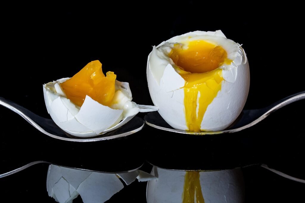 Two soft boiled eggs with runny yellow yolks resting on spoons against a black background