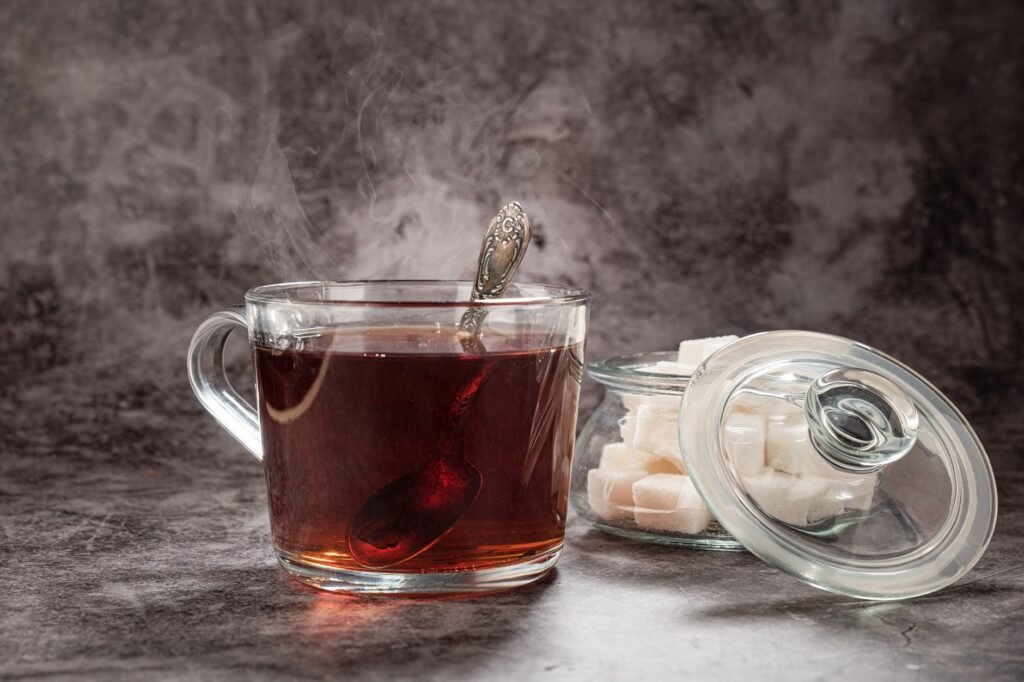 Steaming glass mug of black tea next to a jar of sugar cubes