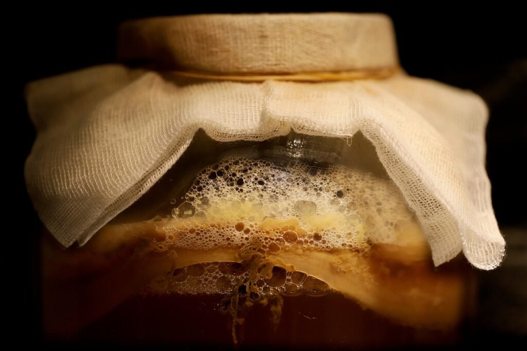 Glass jar of fermenting tea with a foamy top covered by a cloth