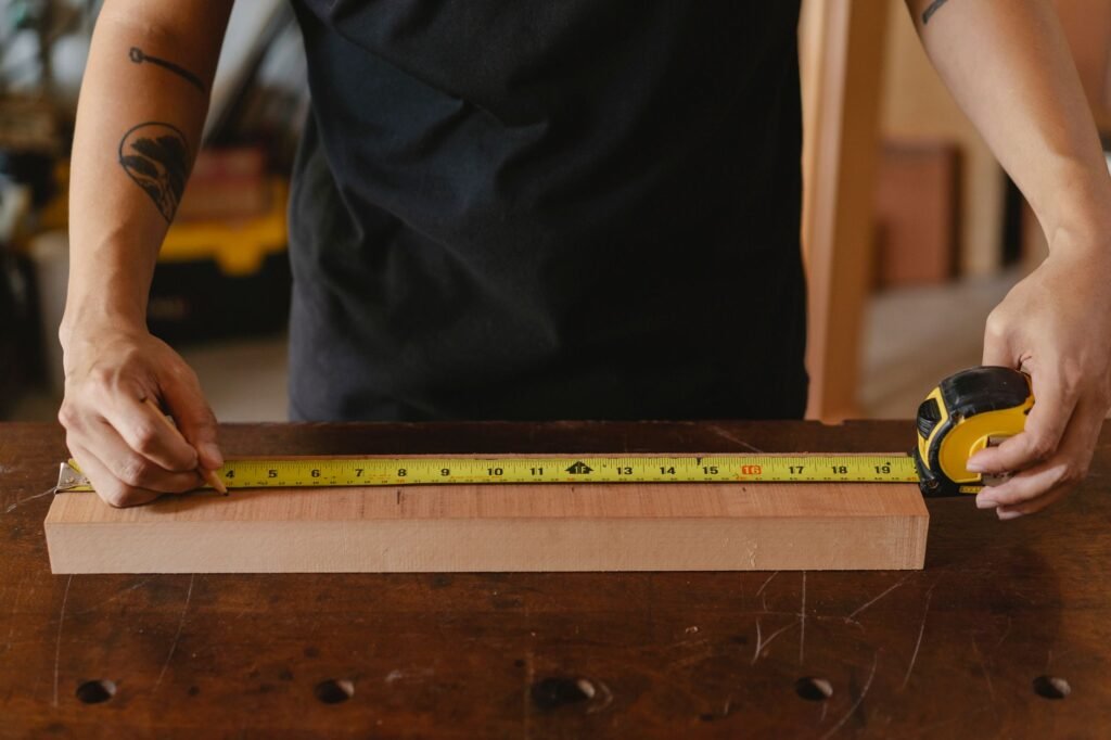 Hands stretching a yellow tape measure along a wooden board on a workbench