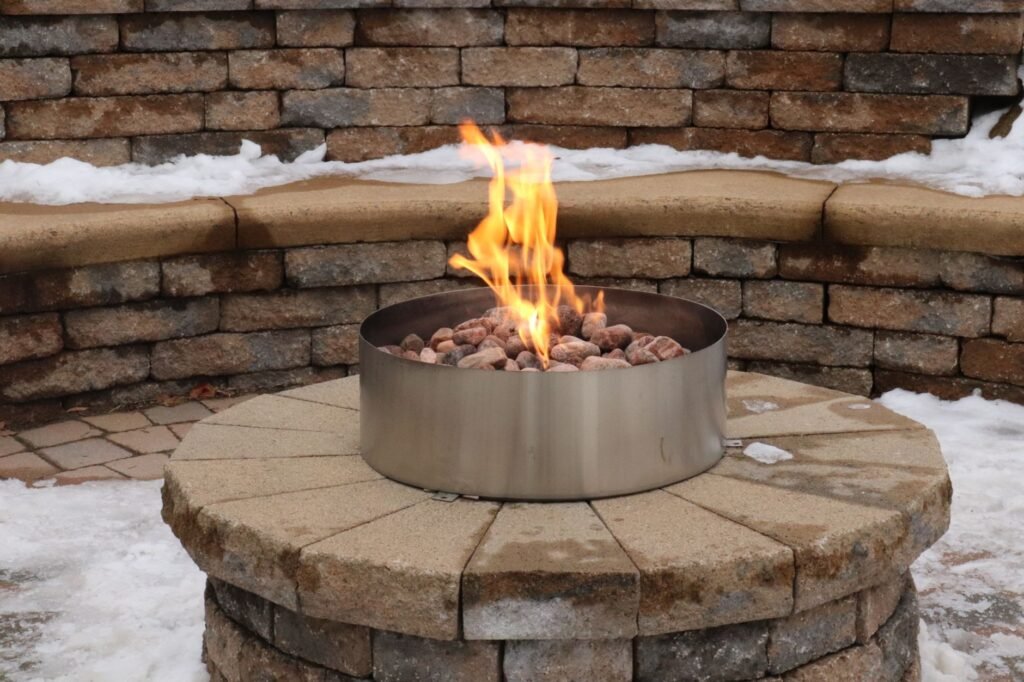 Steel fire ring with lava rocks and a small flame set into a round stone pedestal in snow