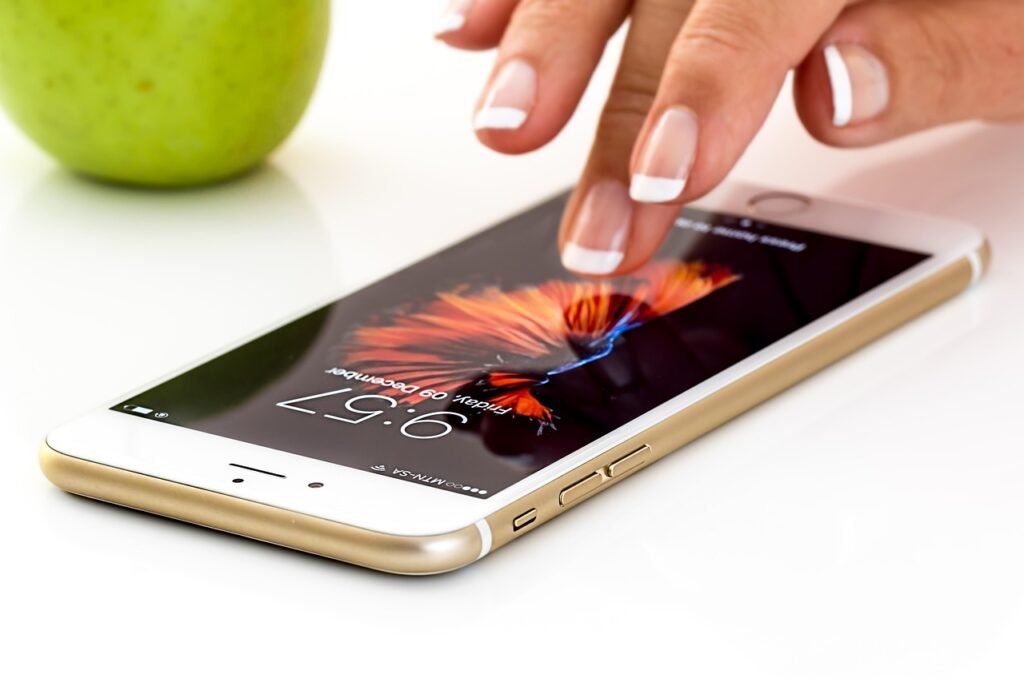 Finger tapping the screen of a smartphone lying on a white table beside a green apple
