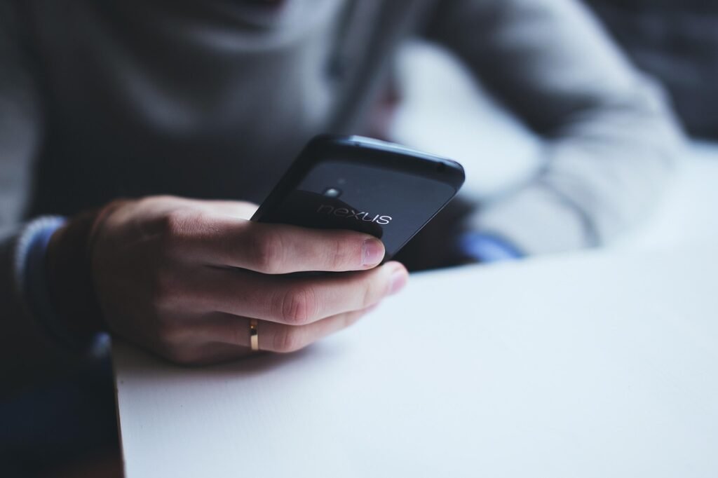 Hands holding a black smartphone above a white table in soft light