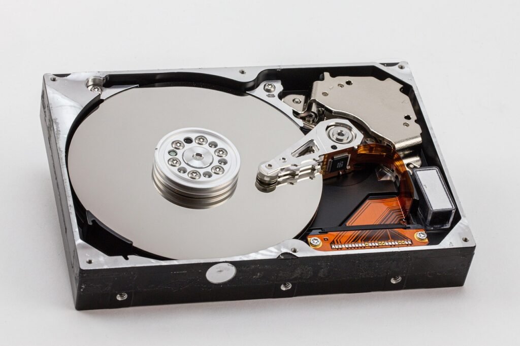 Opened hard disk drive showing its shiny platter, spindle and read arm on a white surface