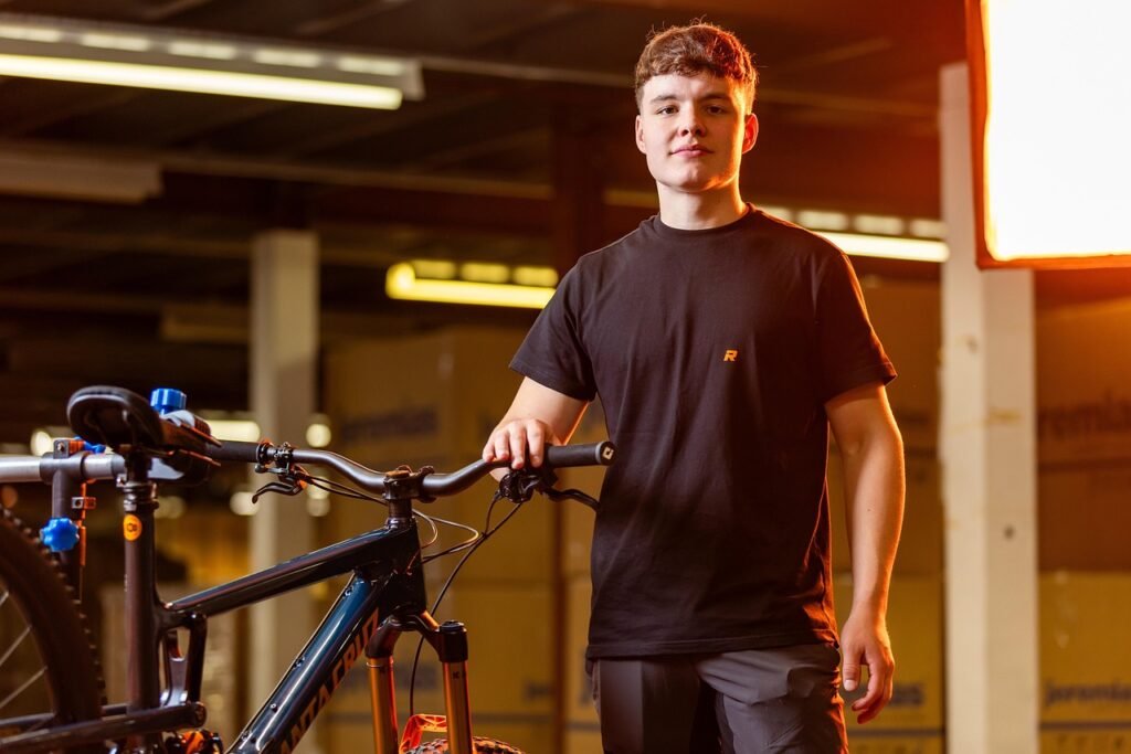 Young man standing beside a mountain bike in a garage with one hand on the handlebar