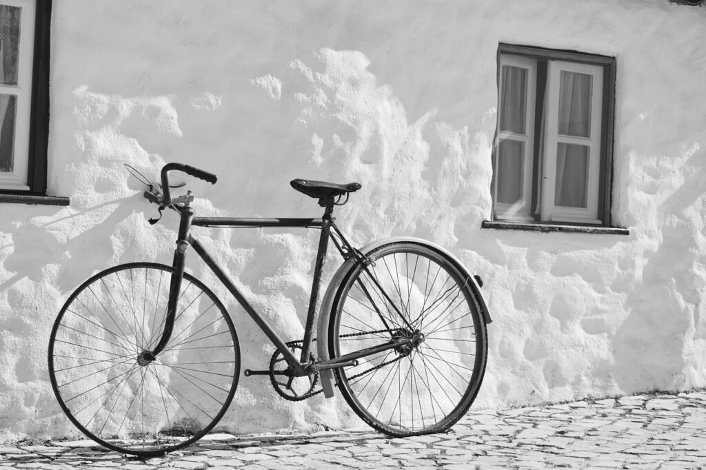 Vintage bicycle leaning against a textured white wall below a window in black and white