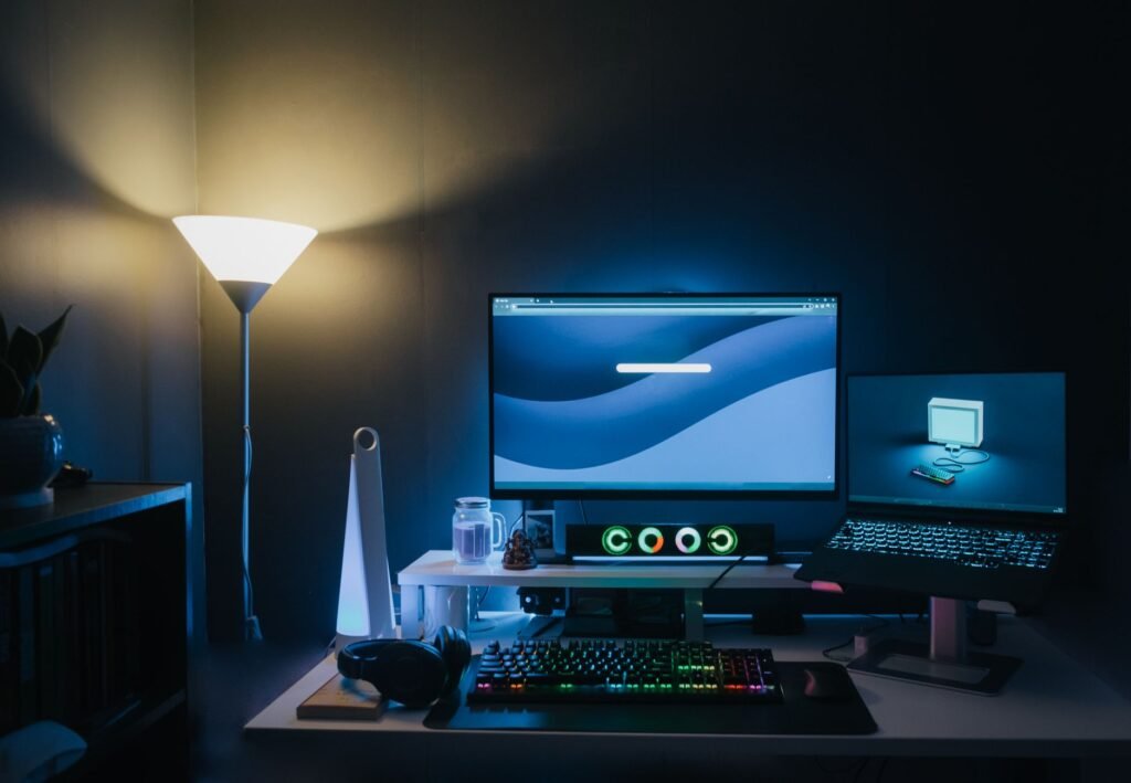 Monitor on a desk with a glowing rainbow keyboard, floor lamp and blue ambient lighting