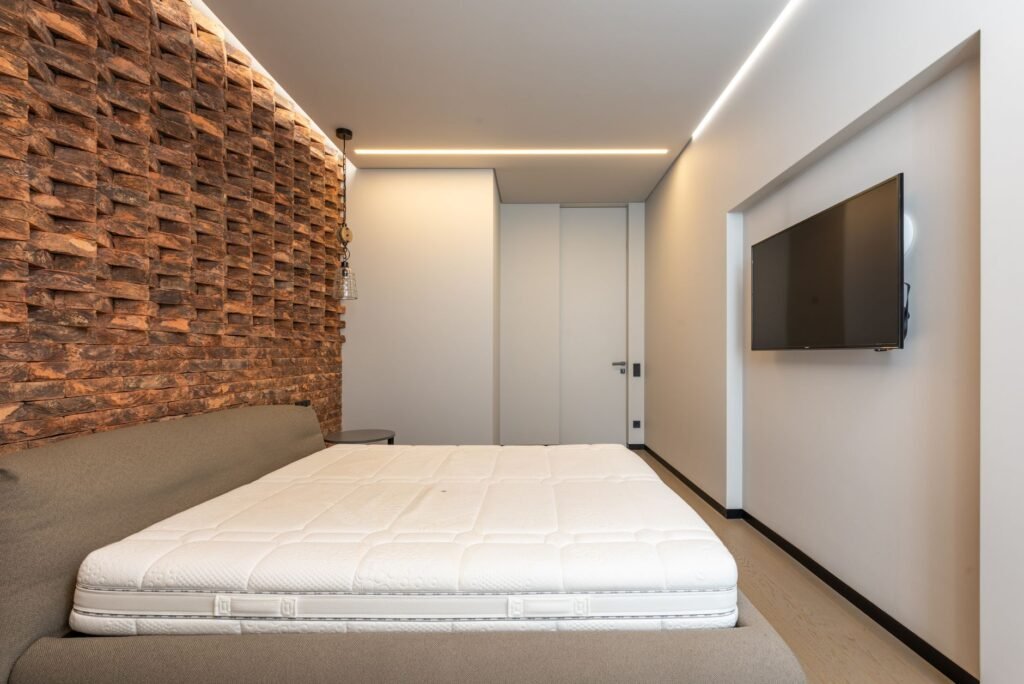 Bare white mattress on a low gray bed frame in a modern bedroom with a textured wall