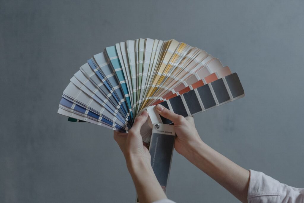 Hands holding a fanned deck of paint color swatches against a gray wall