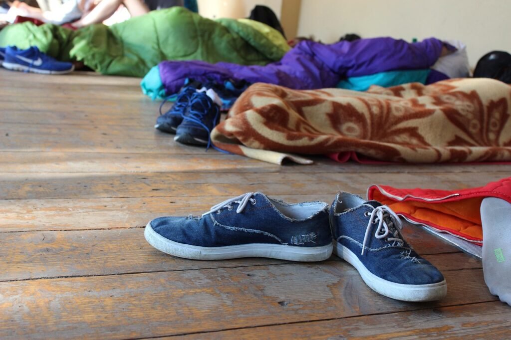 Several sleeping bags spread across a wooden floor with a pair of sneakers in front
