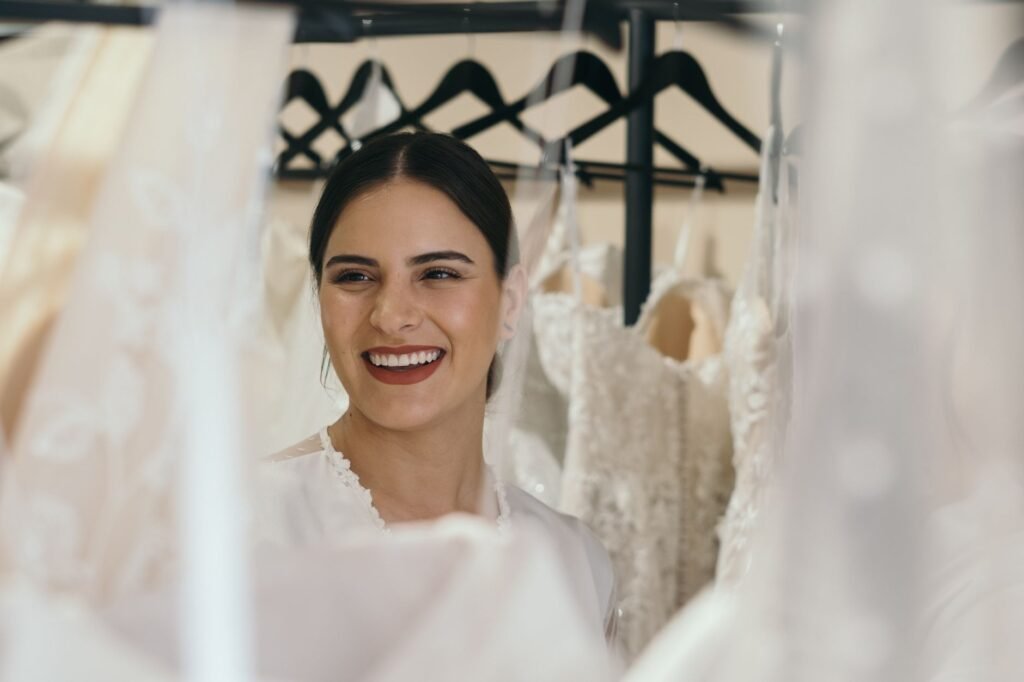 A joyful bride smiles while surrounded by beautiful wedding dresses on hangers.