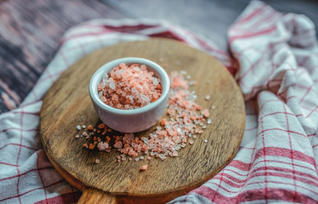 Small bowl of coarse pink salt scattered across a round wooden board on a checked towel