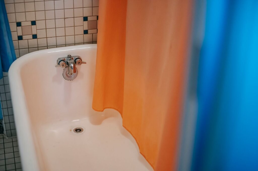 Orange and blue shower curtain pulled across a white tub with a tiled wall behind