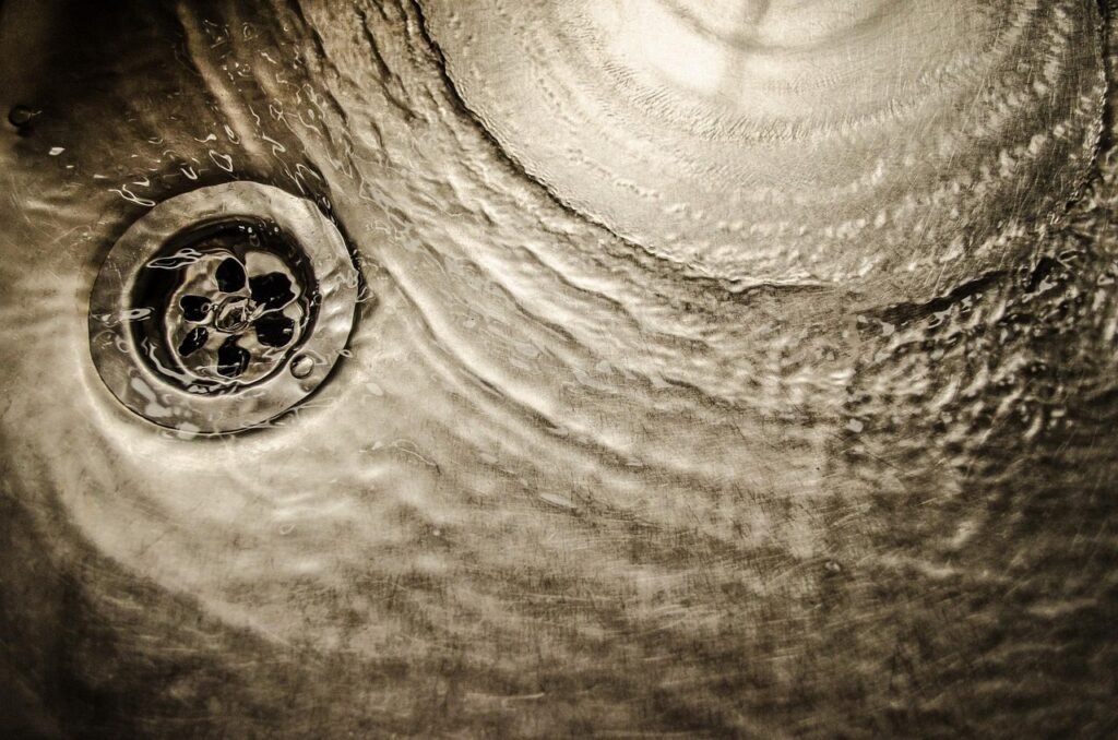 Water swirling in a metal sink around a round perforated drain