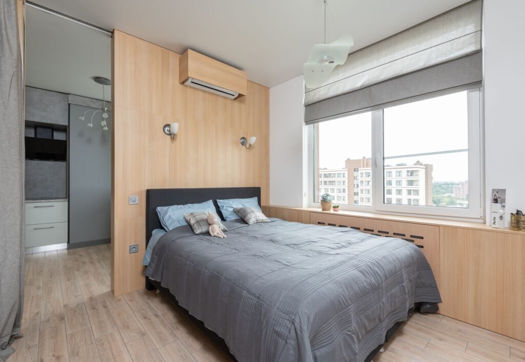 Interior of light modern apartment with bed near window and jalousie with windowsill with decorative elemen...
