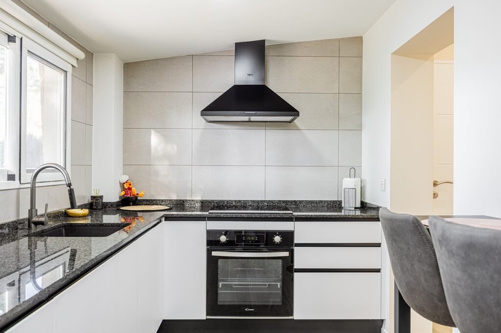 Black oven built in below a cooktop and range hood in a bright white kitchen