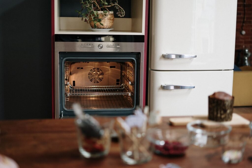Built in wall oven with its light on beside a cream retro refrigerator in a kitchen