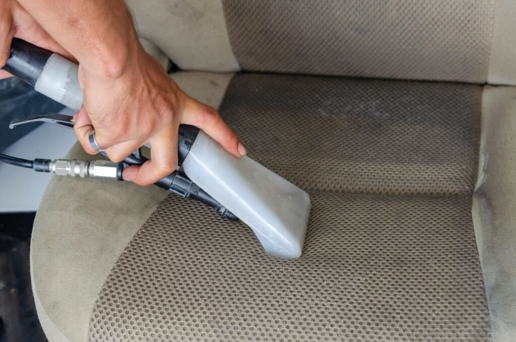 Hand guiding an upholstery extractor nozzle across a gray fabric car seat