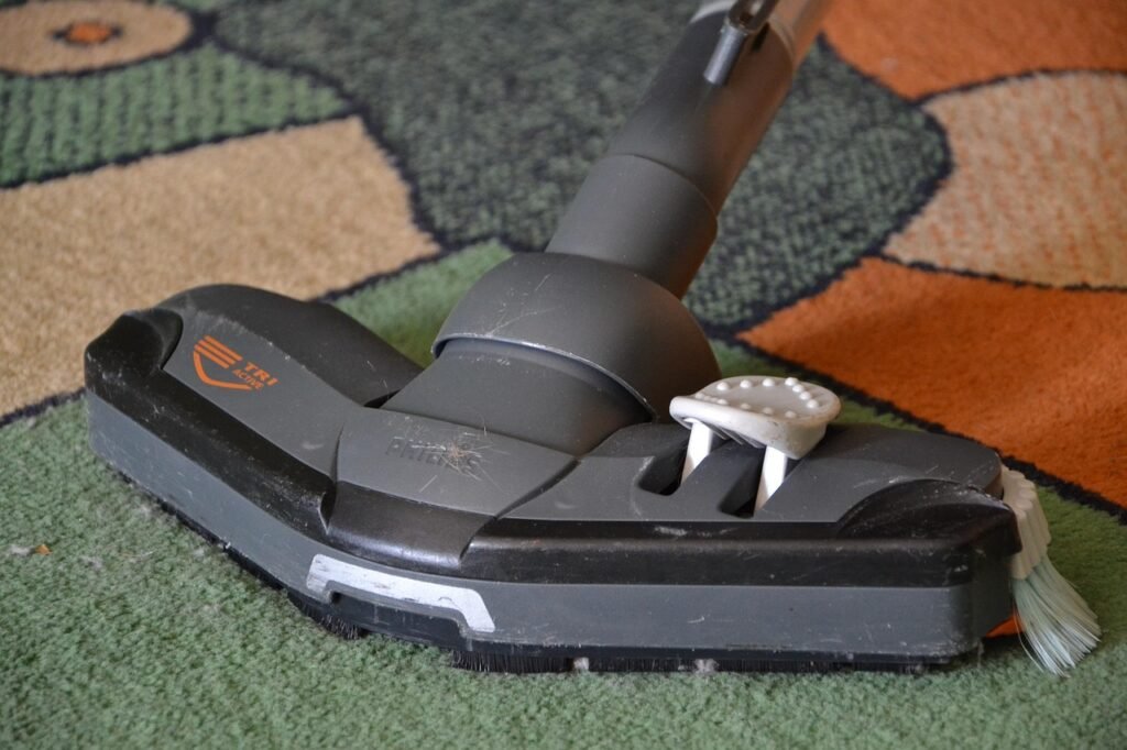 Vacuum cleaner head gliding across a patterned green and orange carpet