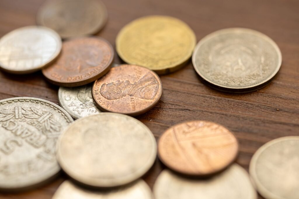 A detailed close-up image showing various vintage coins scattered on a wooden surface, capturing their uniq...
