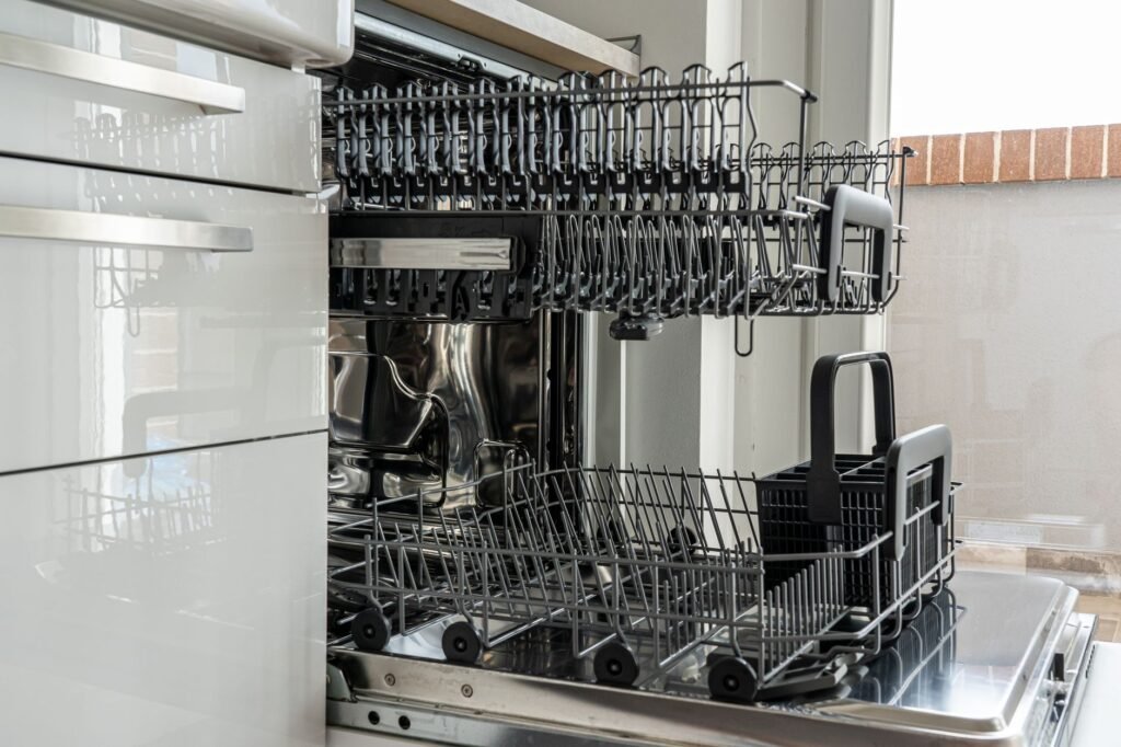 Open empty dishwasher with both racks pulled out in a bright kitchen