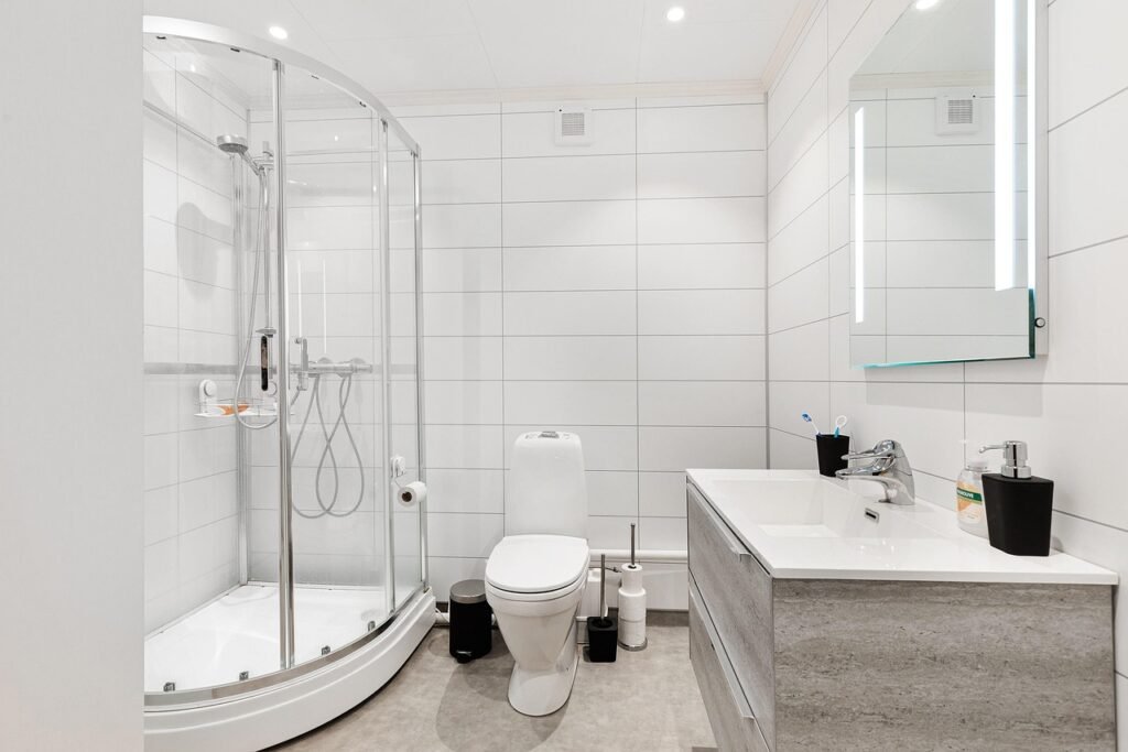 Bright bathroom with white wall tiles, curved glass shower, toilet and vanity sink
