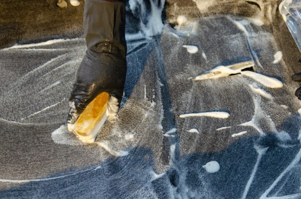 Gloved hand scrubbing soapy dark floor tiles with a stiff bristle brush