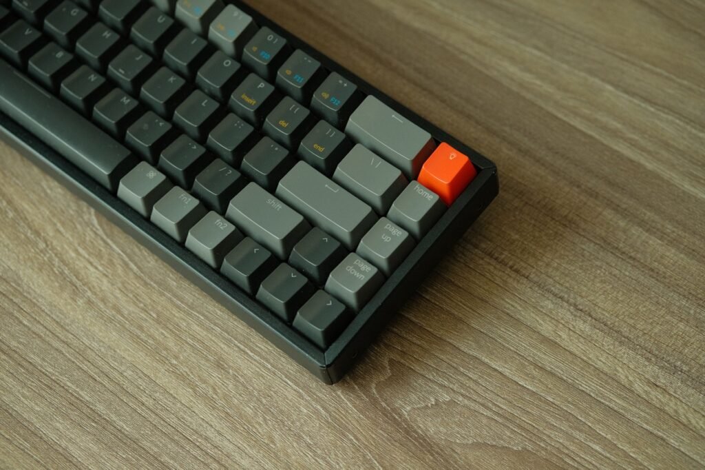 A detailed view of a mechanical keyboard with orange accent key on a wooden table