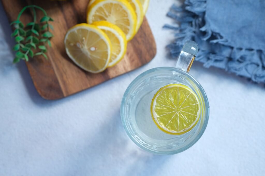 Glass cup of water with a citrus slice beside lemon slices on a wooden board