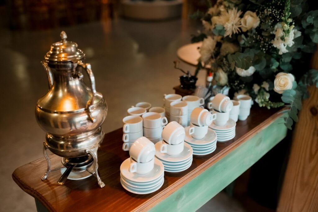 Silver teapot and stacked teacups arranged with white floral decor on a wooden table indoors