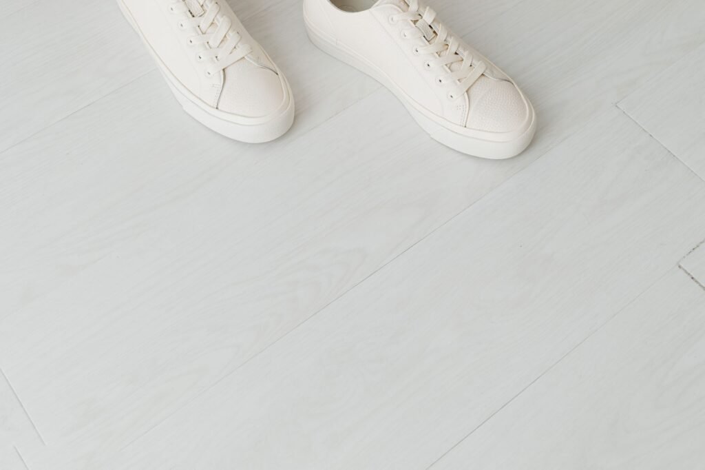 Minimalist white sneakers placed on a modern light wooden floor, captured from above