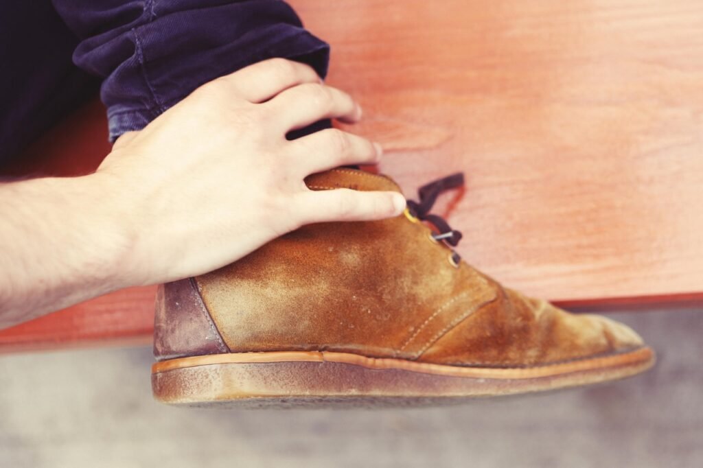 Hand resting on a worn tan suede ankle boot with scuffs and water marks
