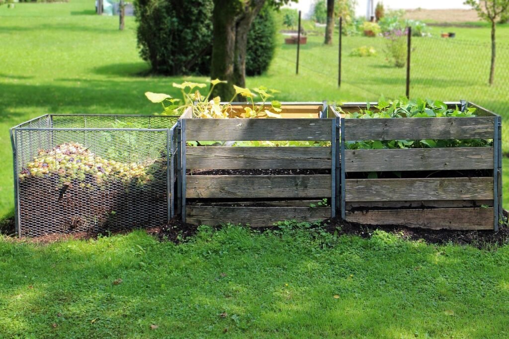 Wooden and wire mesh compost bins standing on a green lawn in a backyard