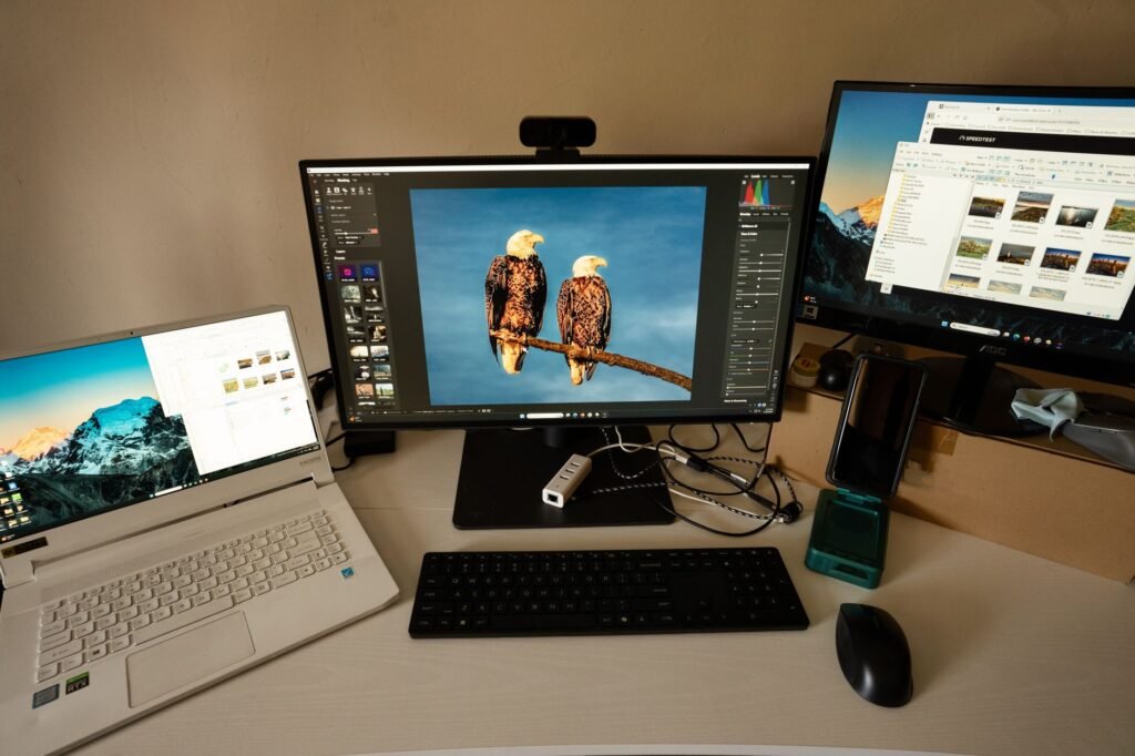Laptop beside two desktop monitors with a keyboard and mouse on a home office desk