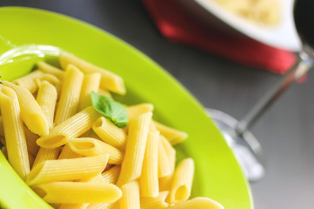 Plain cooked penne pasta with a basil leaf on a bright green plate