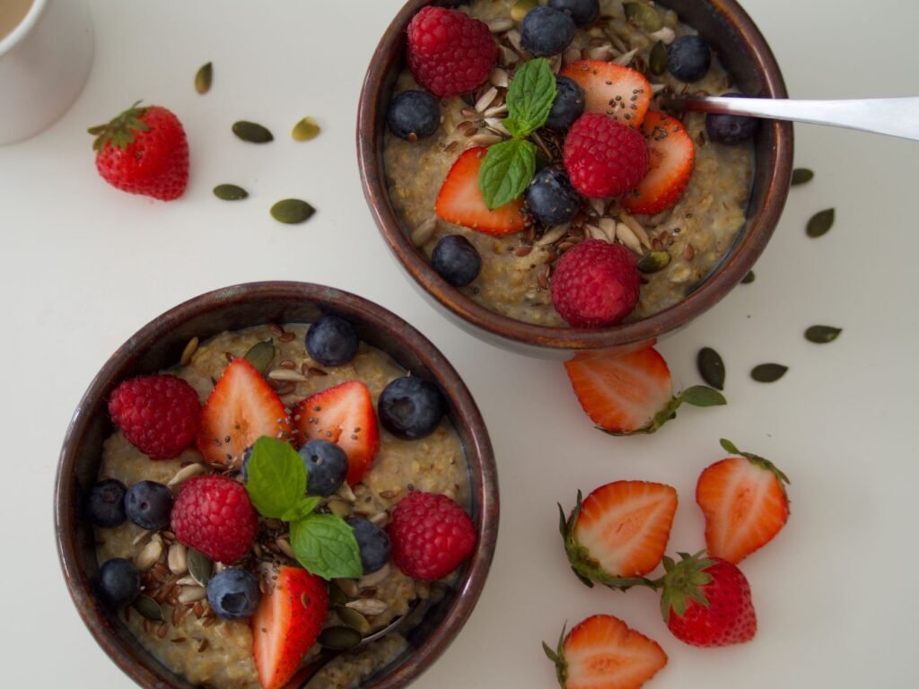 Two bowls of hearty oatmeal topped with strawberries, blueberries and mint leaves on a white table