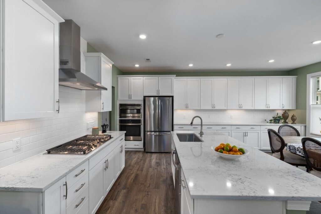 Bright white kitchen with an island, stainless range hood, refrigerator and dark wood floor