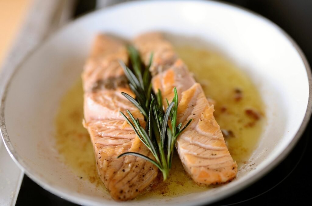 Cooked salmon fillets with a rosemary sprig in a bowl of butter sauce