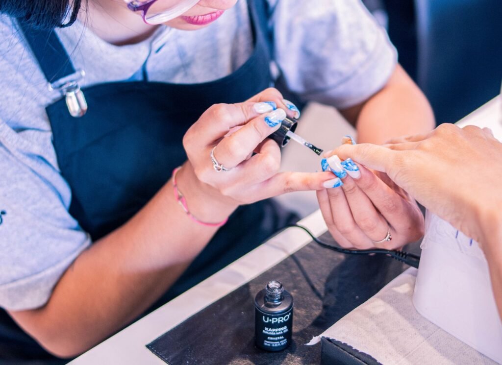 Nail technician painting blue designs onto a client's fingernails with a fine brush
