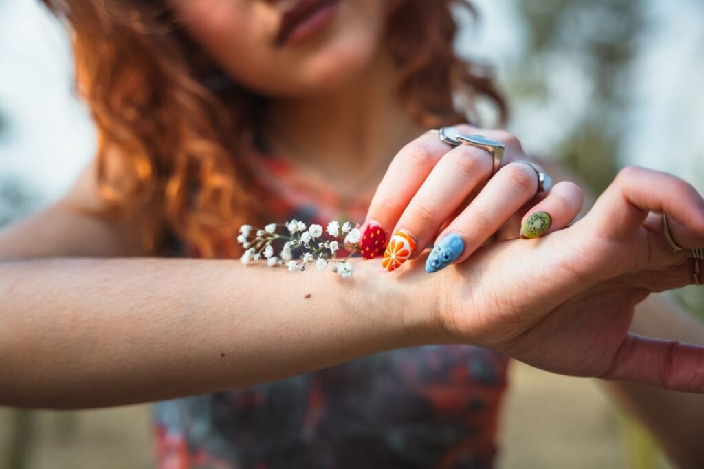 Painted fingernails with strawberry, orange and kiwi designs held beside a sprig of tiny white flowers