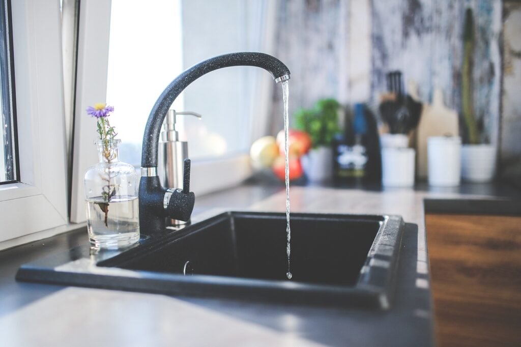 Black gooseneck kitchen faucet running a thin stream of water into a dark sink