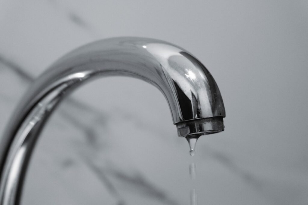 Close up of a curved chrome faucet with a thin stream of water dripping