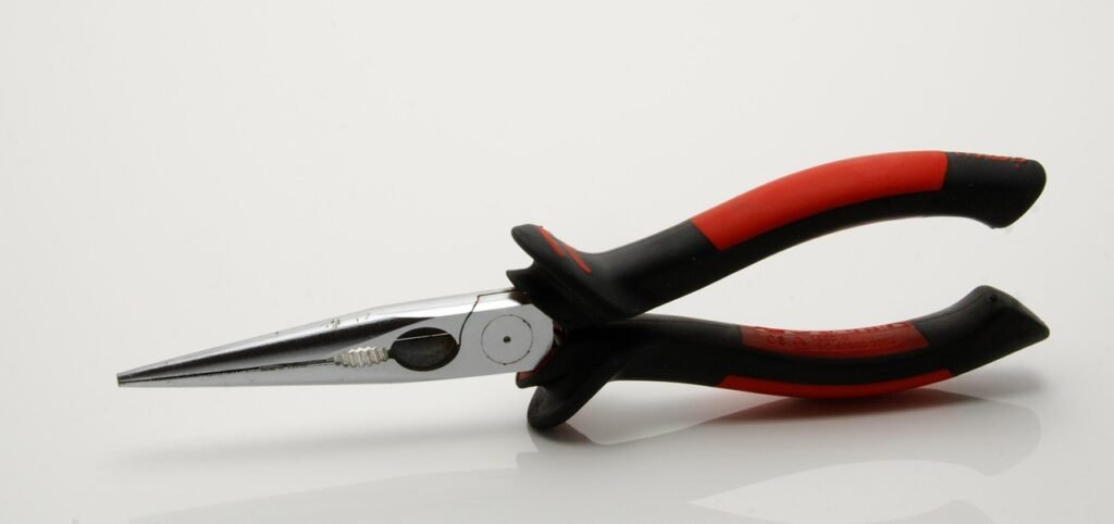 Needle nose pliers with red and black grips on a white surface