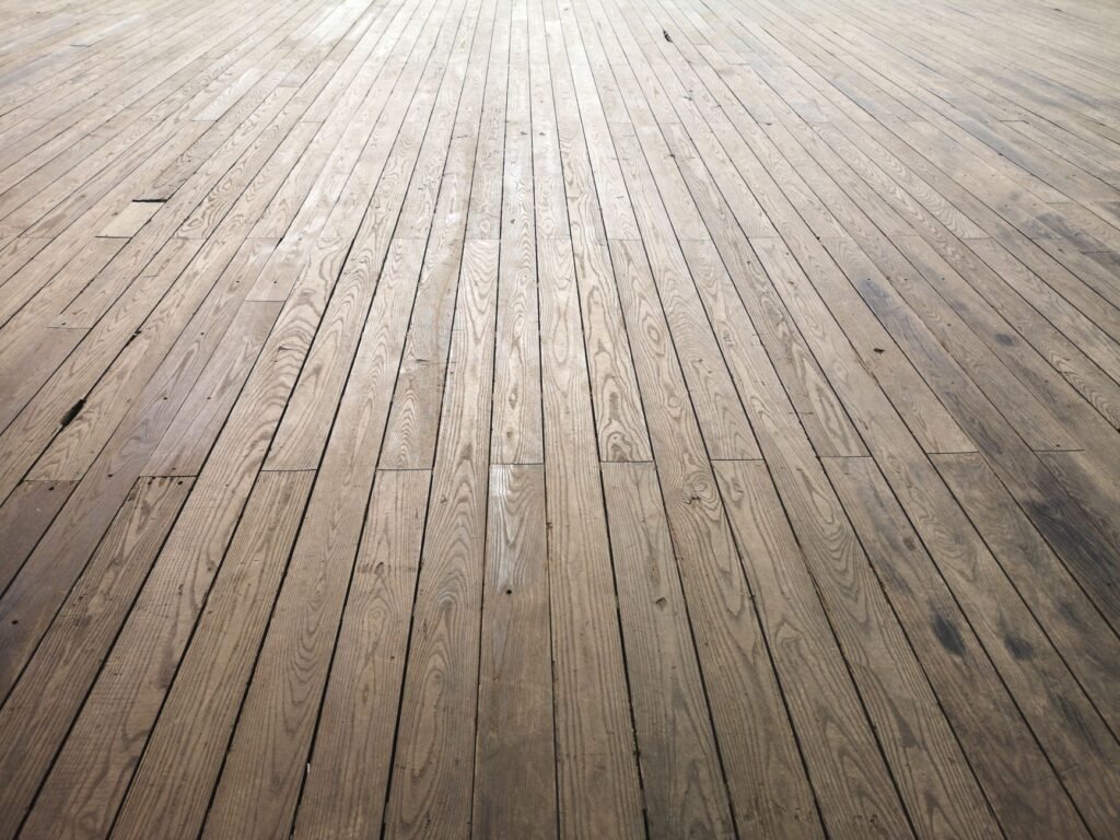 Wide stretch of light hardwood floorboards receding into the distance under soft light