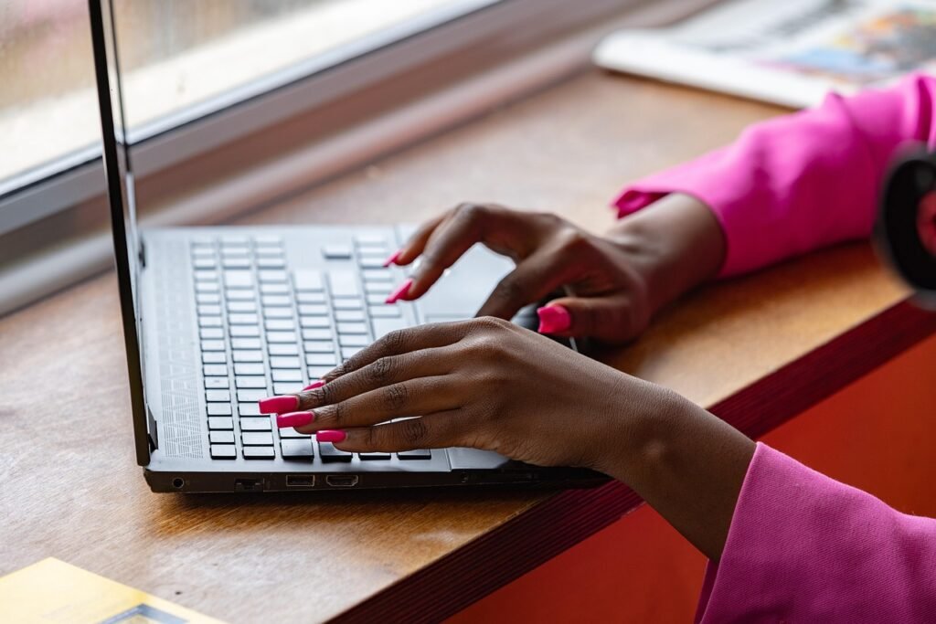 Hands with pink nails typing on a laptop keyboard at a wooden desk