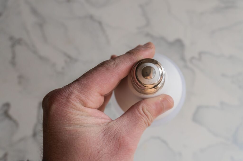 Hand screwing a white light bulb into a ceiling fixture against a marbled ceiling