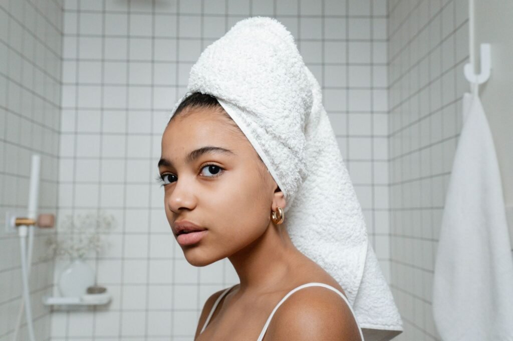 Young woman with wet hair wrapped in a white towel standing in a tiled bathroom