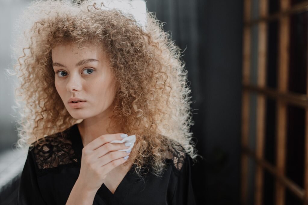 Young woman with voluminous frizzy blonde curly hair looking at the camera indoors