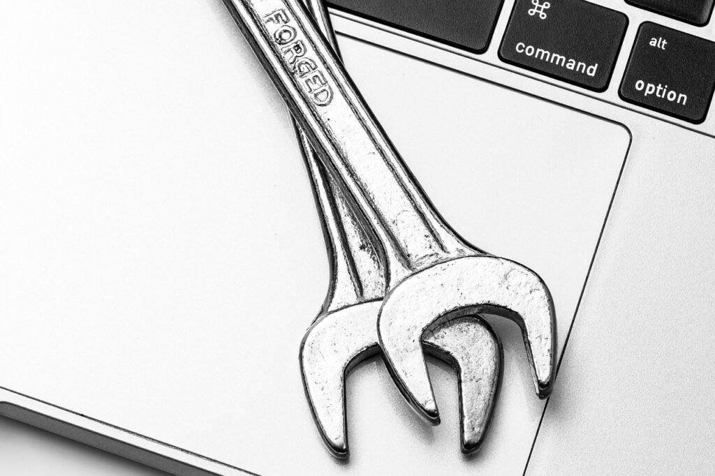 Two metal wrenches resting on a silver laptop beside its keyboard keys